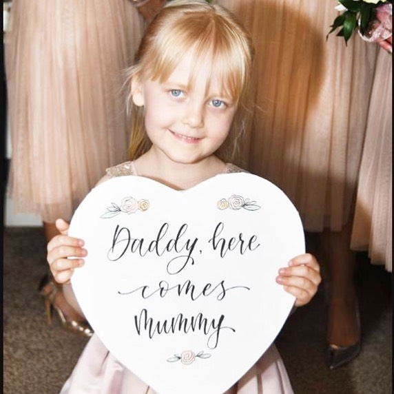 66149248_922507701433863_5060677750612819968_n Girl holding up a sign that reads "Daddy, here comes Mummy."